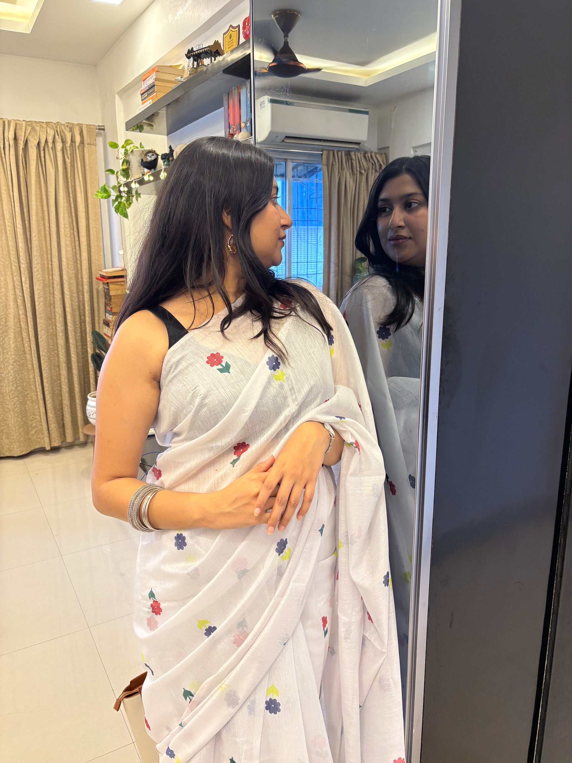 Woman in a white saree with floral patterns standing in front of a mirror. Buy cotton saree.
