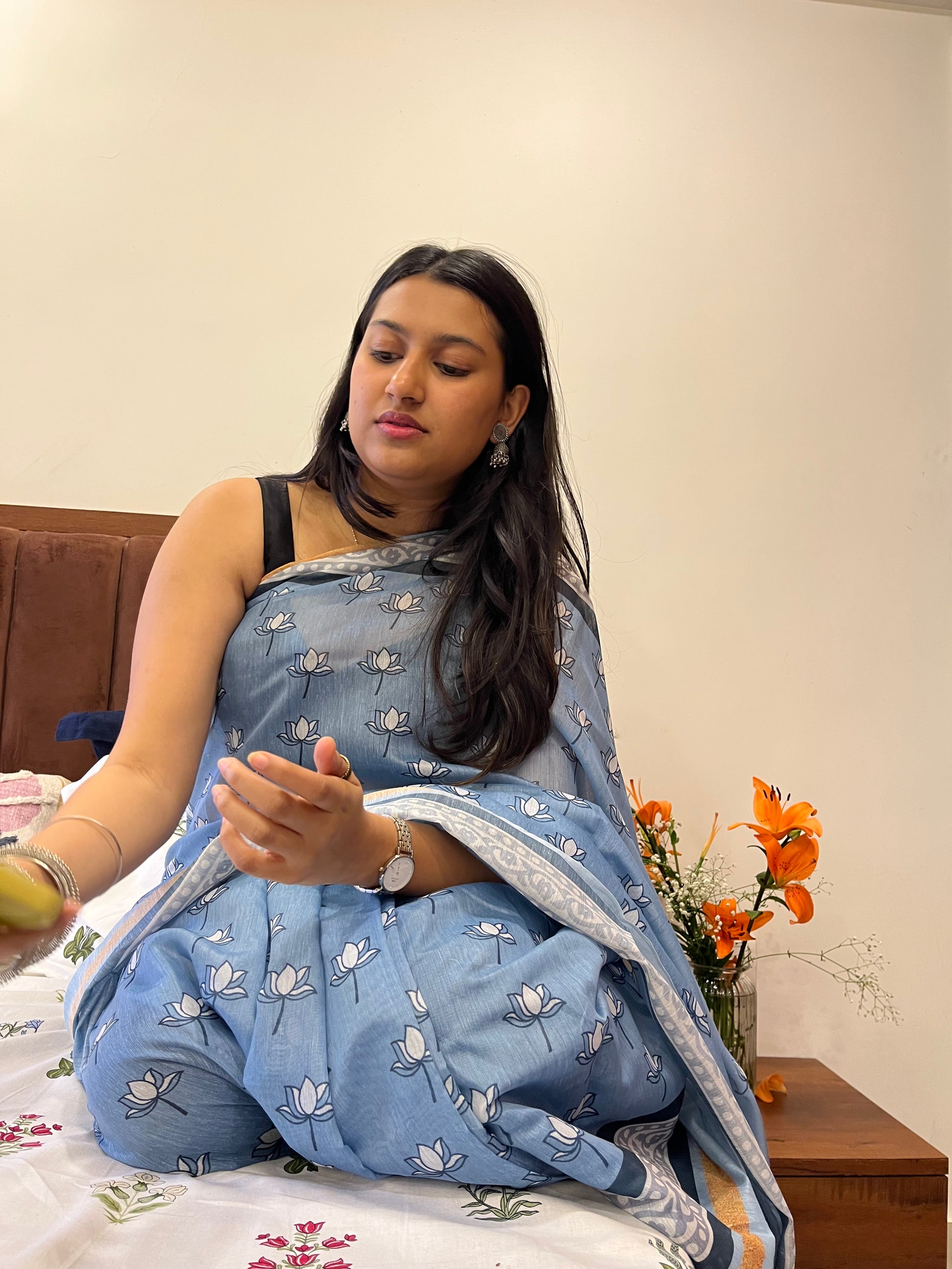 Woman in a blue saree sitting on a couch with a neutral background. Soft cotton saree with lotus print. softest cotton sari. 